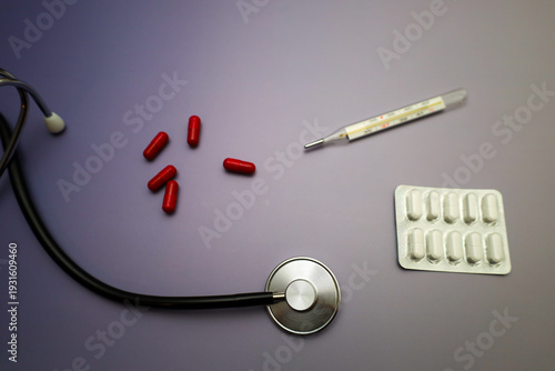 Fotografía A professional medical still life featuring a black stethoscope, a glass thermometer, and various medications on a calm purple background