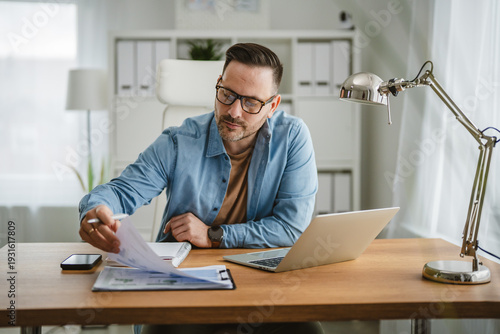 Fotografija Man wearing eyeglasses checking business paperwork at home office