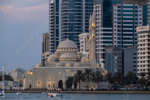 Sunset skyline of Sharjah city with Al Noor Mosque, modern skyscrapers and Khalid Lagoon waterfront under a colorful sky, United Arab Emirates.