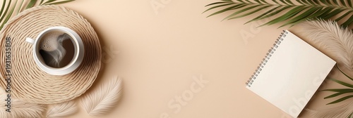 Flat lay of coffee cup on woven mat with notebook, palm leaf, and feathers on beige background