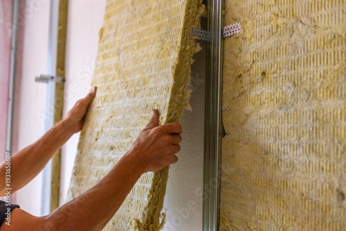 Worker insulating a room wall with mineral rock wool thermal insulation.