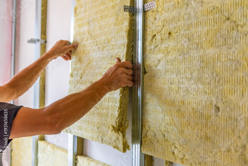 Worker insulating a room wall with mineral rock wool thermal insulation.