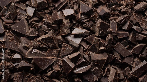 Broken crushed dark chocolate bits on background rotates, close up. Sweet food