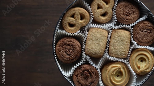 Crispy crumbly shortbread cookies in a round metal box on wooden table, top view, close up, rotates
