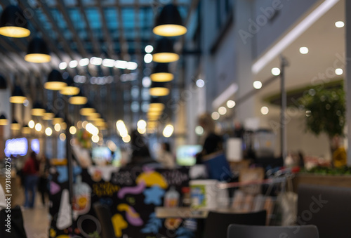 blurred interior of a modern industrial cafe and food court with rows of hanging warm pendant lights and colorful wall art for urban lifestyle background.