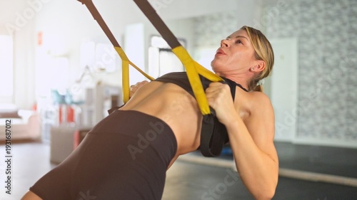 Obraz na płótnie Woman training upper body with suspension straps in gym