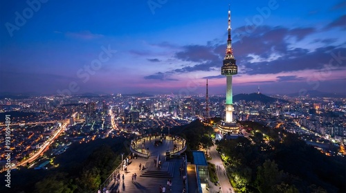 The scene shows a view of the city from Namsan Mountain at night. People walk around while the N Seoul Tower stands tall. The city lights glow as the sky turns dark with clouds