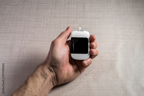 Close up of a man hands using a digital glucose meter to check blood sugar levels at home. Concept of diabetes management, medical self-testing, and healthcare monitoring for a healthy lifestyle.