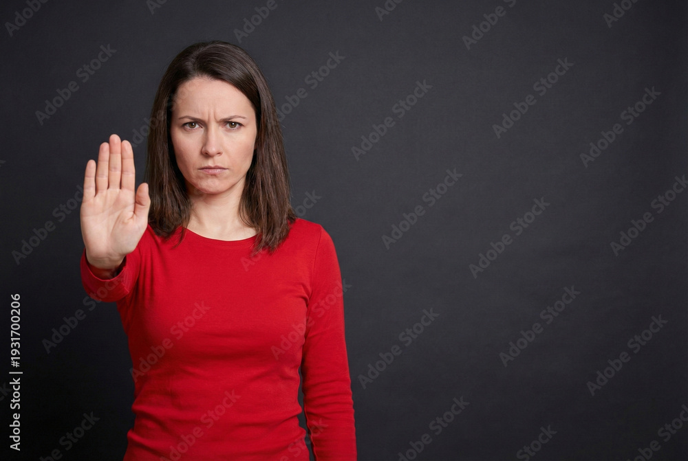 Fototapeta premium Frustrated Woman Showing Stop Hand Gesture Against Dark Gray Background, Expressing Disagreement or Warning