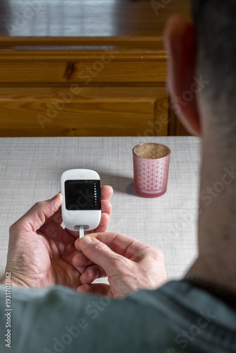 Close up of a man hands using a digital glucose meter to check blood sugar levels at home. Concept of diabetes management, medical self-testing, and healthcare monitoring for a healthy lifestyle.