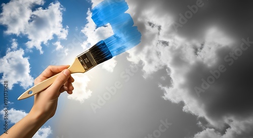 Hand holding paintbrush painting blue sky with white clouds turning to dark gray stormy weather