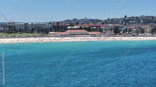 flying along and away central part of famous Bondi Beach, with many people sunbathing and swimming in the pool - 4k aerial video footage