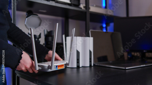 Tableau sur toile Hands adjusting a wireless router with mesh network devices and laptop in backgr