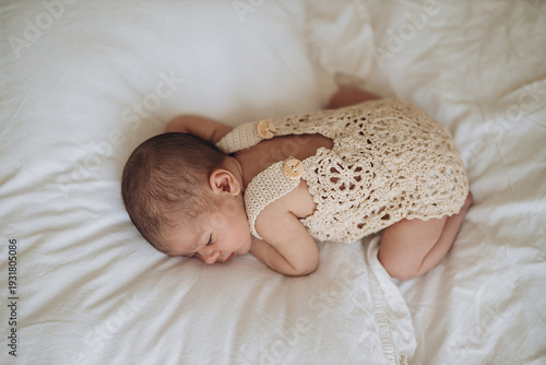Newborn baby sleeping peacefully on soft white bedding in cozy handmade outfit