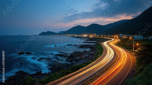 Dusk view: winding coastal road, car light trails, city lights, glowing ocean. Ideal for showcasing travel, speed, motion, and unique coastal phenomena.