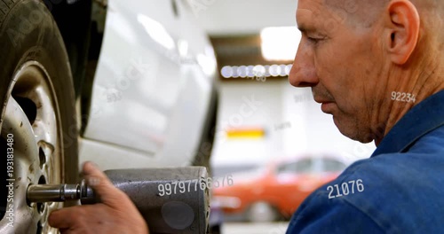 Auto mechanic engaging wrench, loosening lug nut for wheel removal, graphics appearing over wheel