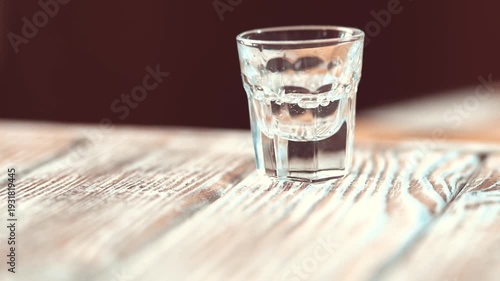 Crystal clear vodka pouring into a shot glass on a table.