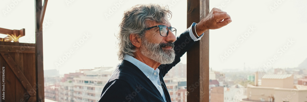 Obraz premium Senior enjoys the view standing on the balcony with mobile phone in hand. Panoramic