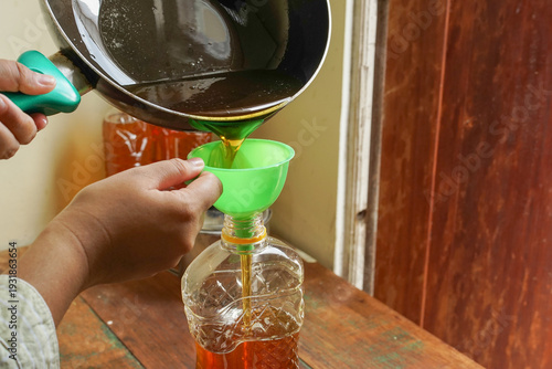 фотографія Close up person hand pouring used cooking oil from frying pan into plastic bottl