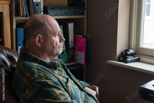 Retired man staring out of a window in contemplation