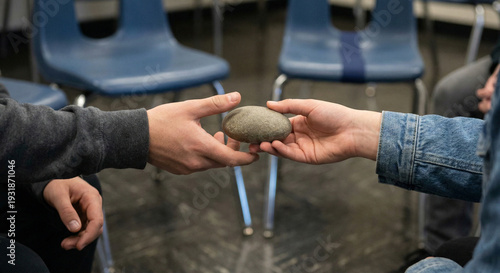 Hands passing a smooth stone in a circle of chairs