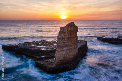 Rock formation at sunset on Four Mile Beach in Santa Cruz California with ocean waves swirling around coastal cliffs under a golden sky