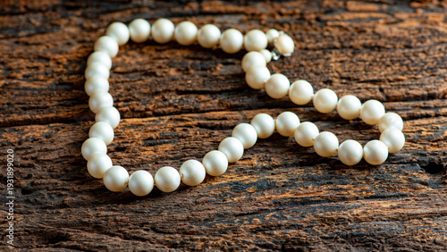 Pearl necklace, a beautiful, stage-prop pearl necklace positioned on very rustic wood against a dark background, selective focus.