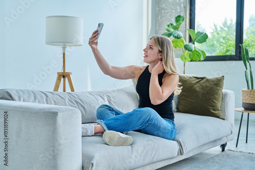 Young woman taking selfie photo using smartphone sitting on floor at home