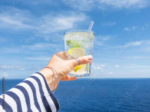 Φωτογραφία Hand holding a glass of drink against a bright blue sky