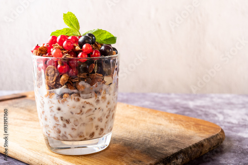 Healthy granola with milk, fresh red and black currants, and mint in a glass.