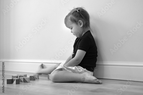 Canvas Print A child's emotions, a sad little girl sitting turned away on the floor, adapting