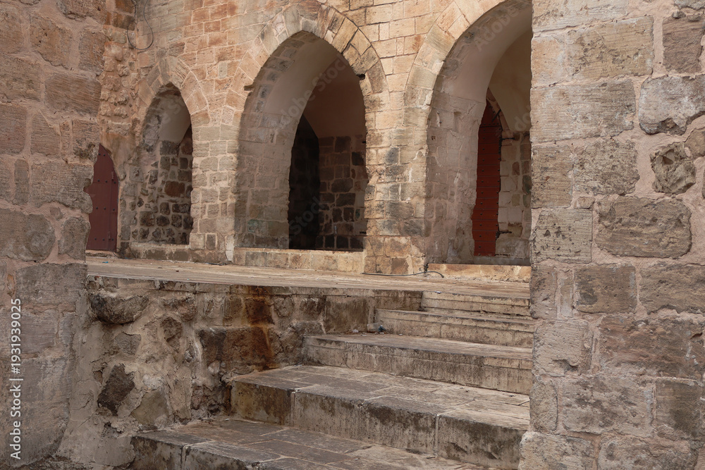 Fototapeta premium Foggy Historic Stone Street in Old Town Mardin, Turkey,Misty historic stone street in the old town of Mardin, Turkey. Traditional limestone buildings with arches and narrow alleyway disappearing into 