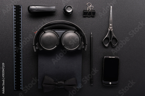 Flat lay of black stationery arranged as a man's silhouette with headphones and bow tie.