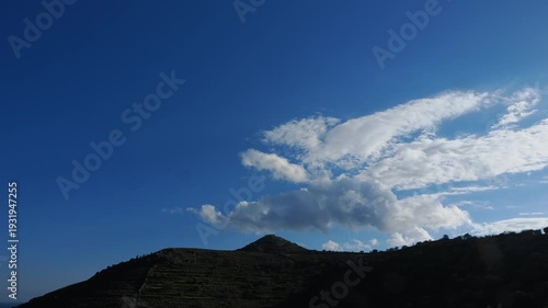 4K timelapse footage of fast moving clouds forming, shifting and dissipating over a silhouetted island hill in the Cyclades. Dramatic Mediterranean sky with multidirectional cloud movement suitable fo