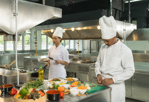 professional chefs white uniform work together clean, modern commercial kitchen. focus prepare various dishes surrounded  stainless steel appliances and fresh ingredients. scene high culinary teamwork