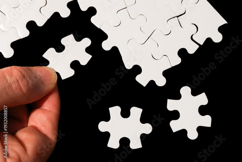 Close-Up of Hand Placing White Jigsaw Puzzle Piece Into Place on Black Background