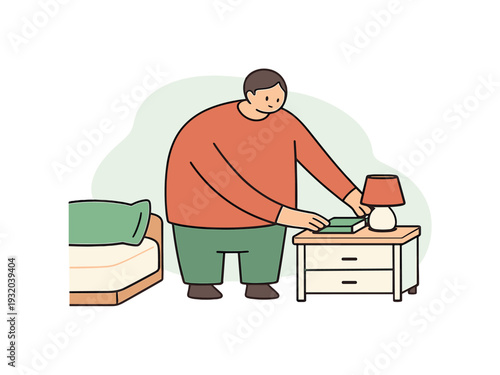 Man placing a book on a bedside table next to a lamp and a bed