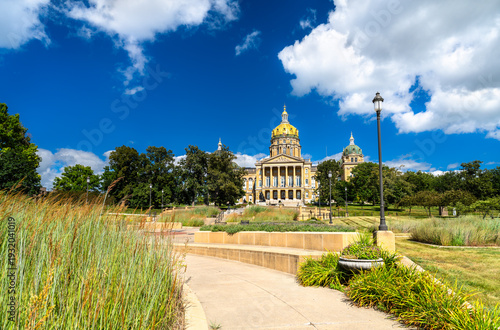 Iowa State Capitol building stands on a hill in Des Moines, USA. Historic architecture features a central golden dome and four corner domes under a blue summer sky