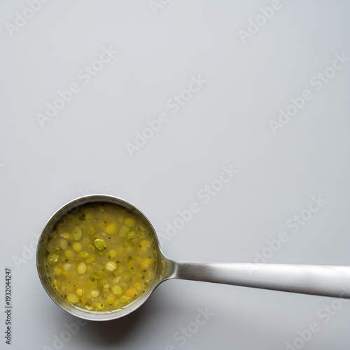 Metal ladle filled with simple split pea soup resting on the lower left edge of a large pale gray background, most of the space left empty as negative space for nutrition or budget cooking text.