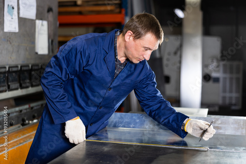 Fotografia Serious middle-aged technician in blue jacket and protective gloves measuring st