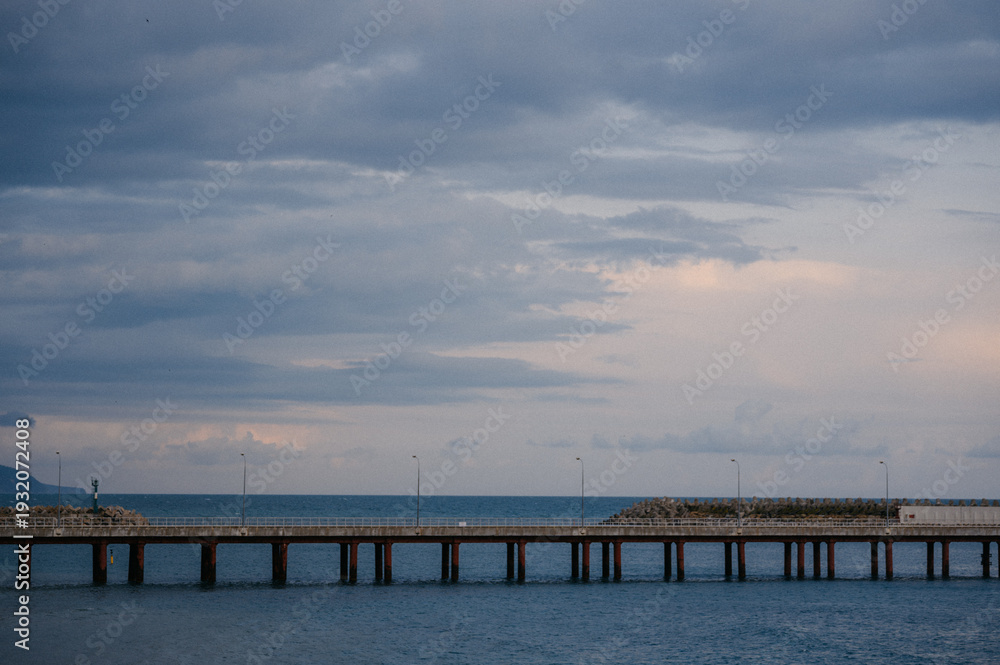 Fototapeta premium Long pier extending over calm ocean waters under cloudy sky