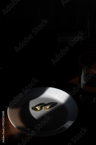 Golden capsules on a white plate with a glass of water, showing a health routine