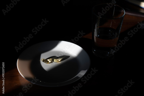 Golden softgel capsules on a white plate with a glass of water, highlighting daily health supplements