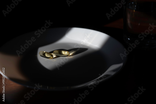 Two omega-3 supplements on a white plate with a glass of water for daily health