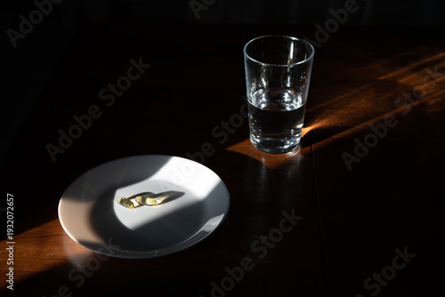 Pills and a glass of water on a table with morning sunlight suggesting health and cure