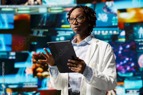 Принти на полотні Scientist analyzing viruses on tablet to support vaccine development, surrounded by medical interfaces videowall backdrop