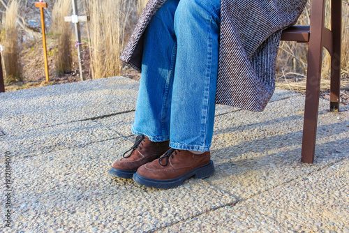 Warsaw, Poland, March 01, 2026. Lower body view of a person resting in blue jeans and brown autumn boots on a sunny terrace. High quality photograph.