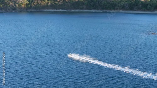 Aerial tracking shot of jet ski in tropical bay at sunset