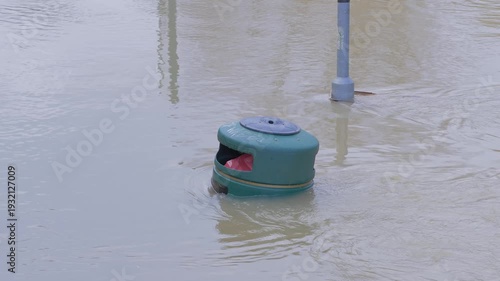 submerged waste refuse rubbish bin and lamppost in fast flowing muddy brown water, swirling currents and eddies