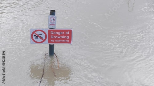 submerged sign in fast flowing river flood, rippling muddy brown water, danger of drowning, no swimming warning